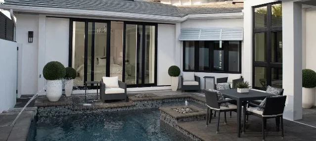 Luxury backyard patio and pool area featuring large black-frame sliding glass doors and matching windows on a modern white house.